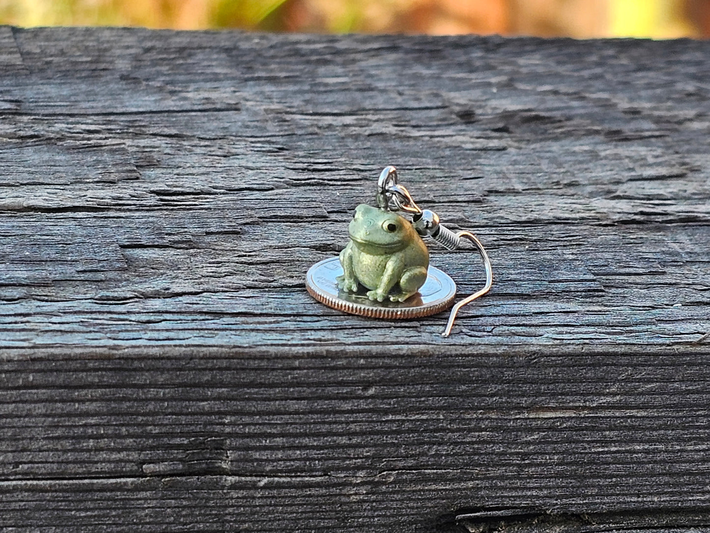 Tiny hand painted frog earring sitting on a coin for size reference – Buck the Frog jewelry by Ghost Cactus Co