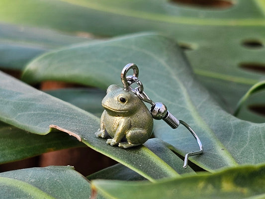 Tiny hand painted frog earring resting on a green leaf – Buck the Frog jewelry by Ghost Cactus Co