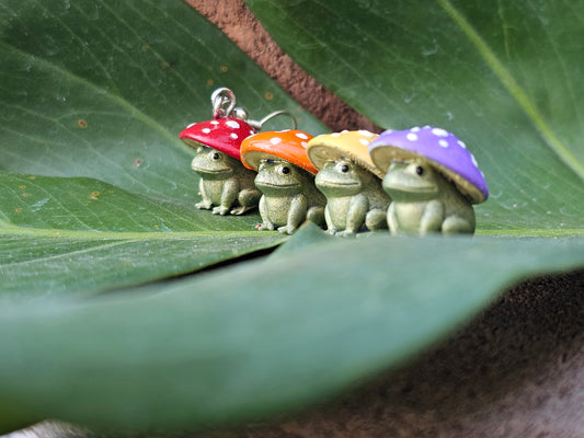 Colorful mushroom frog earrings in red, orange, yellow and lavender displayed on a green leaf